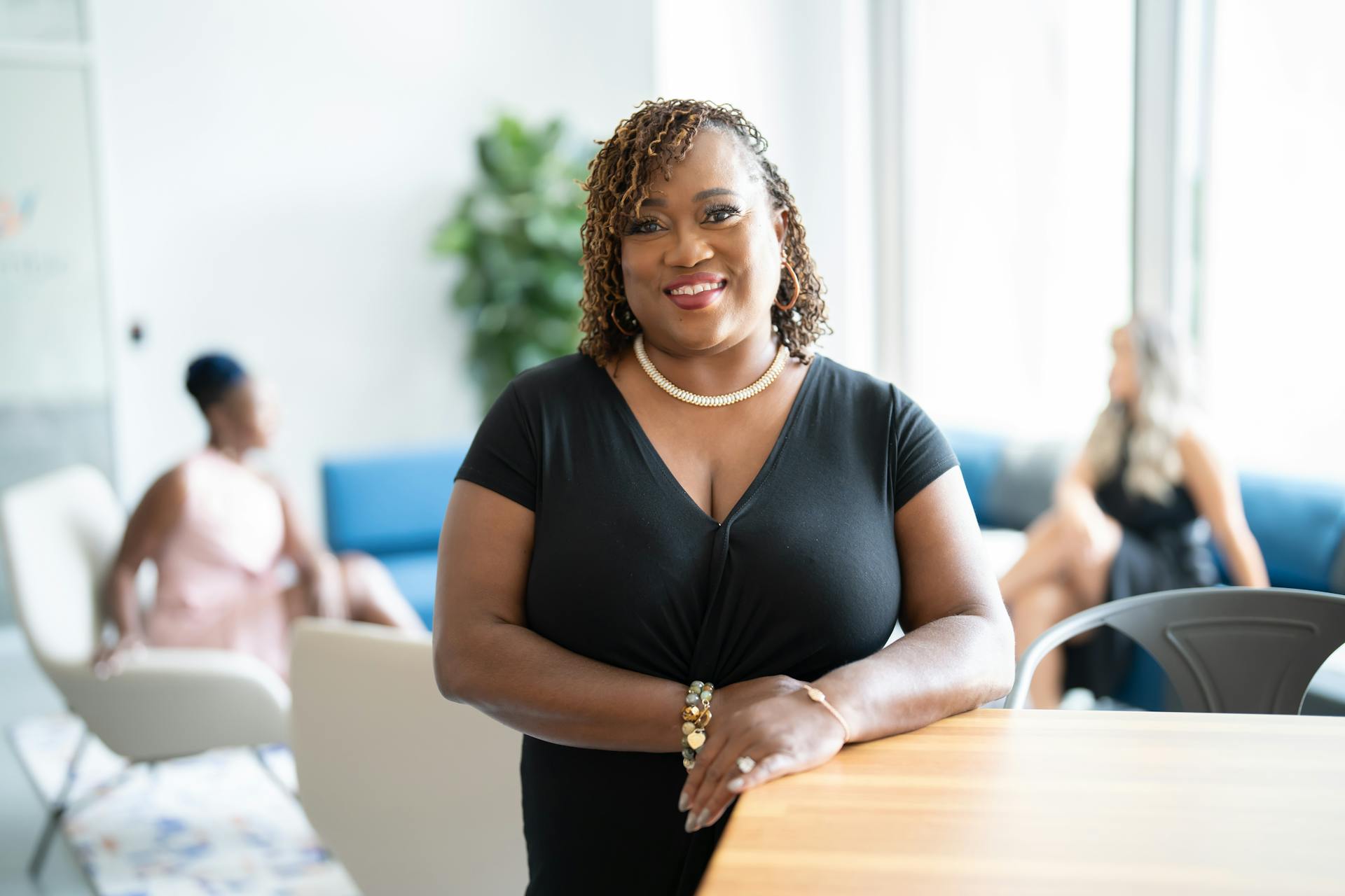 A woman stands beside a desk and smiles at the camera