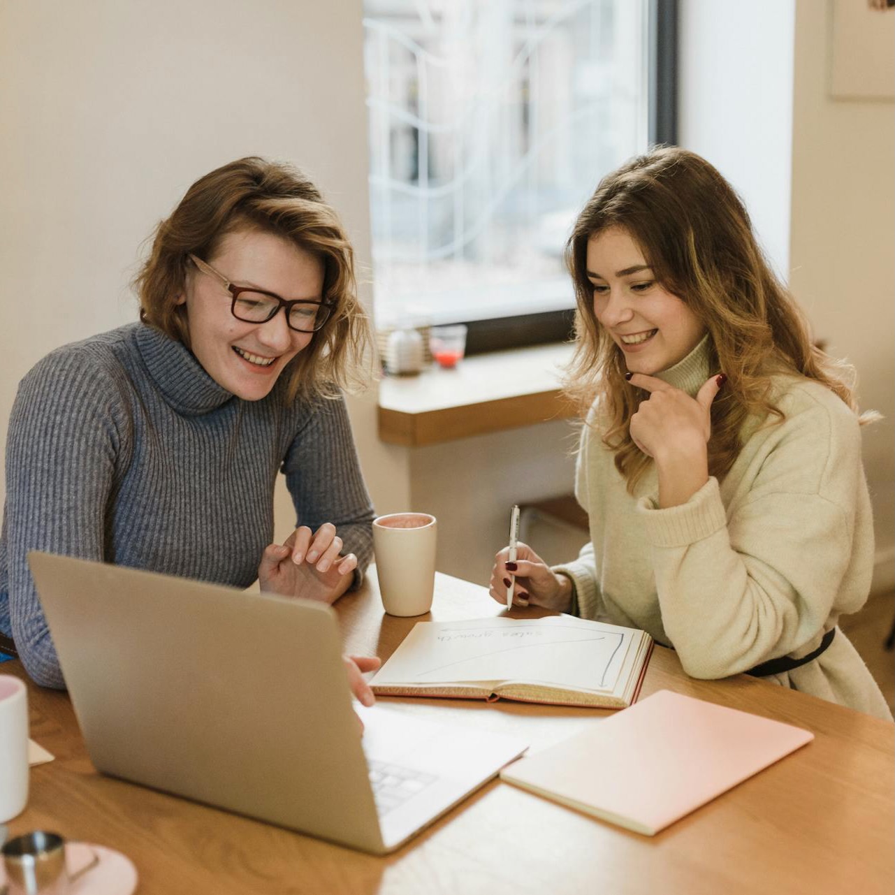 A woman is showing a person something on a computer while they smile and take notes.
